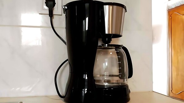 A black coffee maker with a transparent water reservoir and a power cord plugged in.