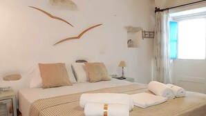 Une chambre d’hôtel bien rangée, avec un lit, des oreillers, une table de chevet avec une lampe et une fenêtre avec des rideaux.