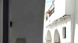 Une rue étroite bordée de bâtiments blancs, avec un trottoir pavé et une chaise au premier plan.