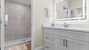 Un baño con cabina de ducha de vidrio, tocador blanco con espejo y un perchero para toallas.