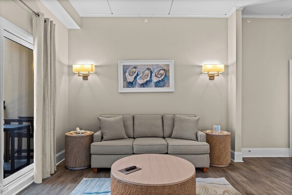 A modern living room with a grey sofa, two side tables, a round coffee table, and a painting of oysters on the wall.