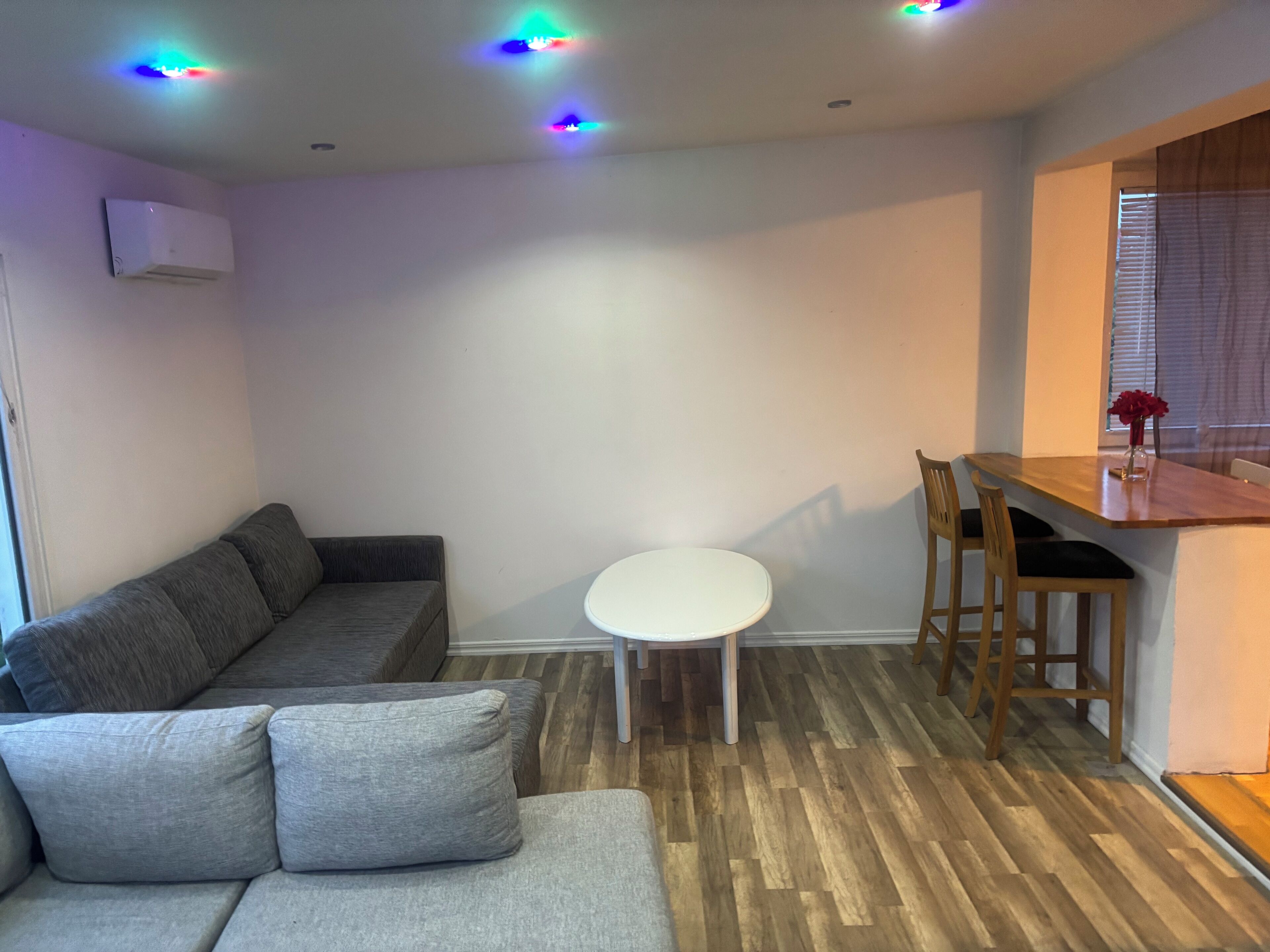 A compact living space with a grey sofa, a small round table, and a wooden dining table.
