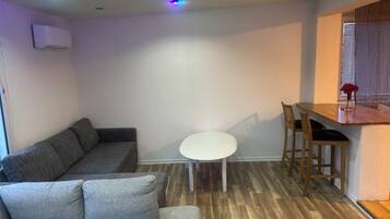 A compact living space with a grey sofa, a small round table, and a wooden dining table.