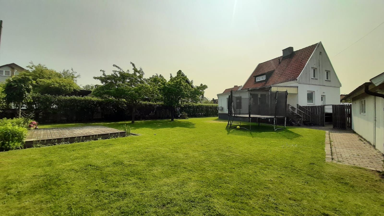 A residential backyard with a well-maintained lawn, a wooden deck, and a house with a sloped roof.