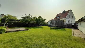 A residential backyard with a well-maintained lawn, a wooden deck, and a house with a sloped roof.