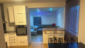 A compact kitchen with modern appliances, a dining area with a wooden table and chairs, and a living room with a sofa and a window. - Charming 4-bedroom house with AC in Skåne län (Skåne län)
