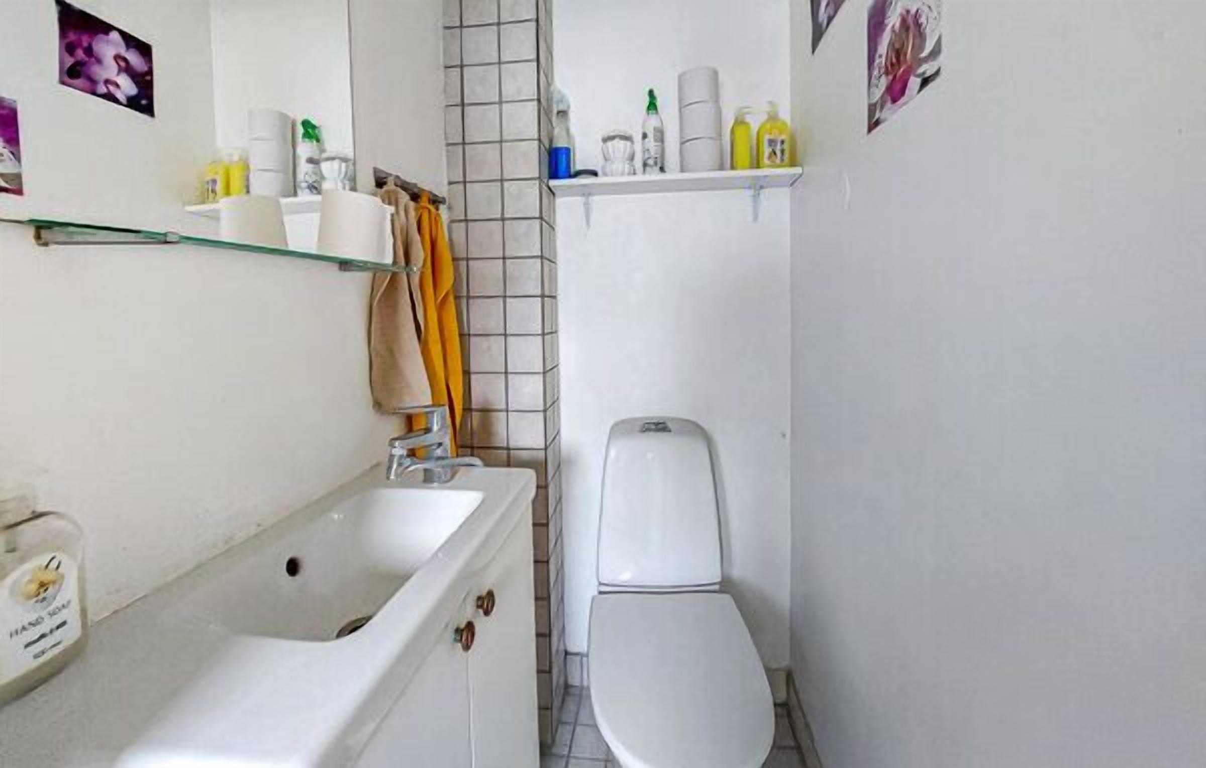 Une petite salle de bain avec un lavabo blanc, des toilettes et une étagère en verre au-dessus des toilettes, où sont rangés les articles de toilette.