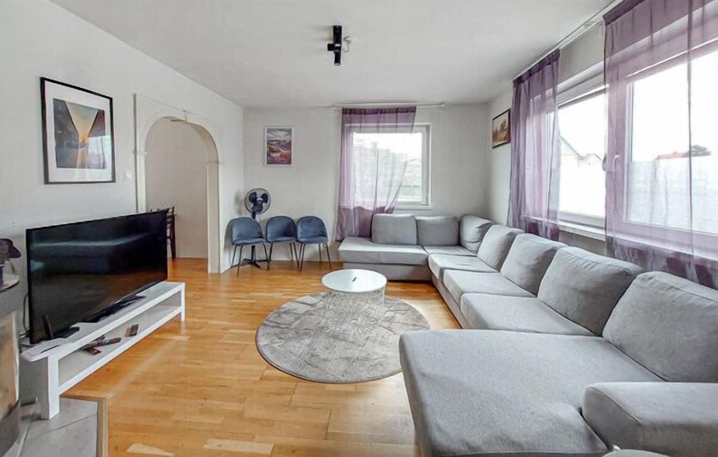 A modern living room with a flat-screen TV, grey sofa, and a round coffee table.