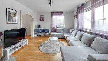 A modern living room with a flat-screen TV, grey sofa, and a round coffee table.