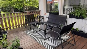 A covered outdoor deck with wooden flooring, a black and white striped rug, and two black chairs. - Charming 4-bedroom house with AC in Skåne län (Skåne län)
