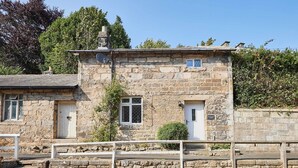 A stone building with two doors and windows, a stone wall, and a wooden fence. - Host & Stay | Brackenrigg Cottage (Rothbury)