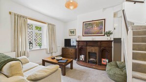 A living room with a fireplace, a sofa, a coffee table, and a staircase. - Host & Stay | Brackenrigg Cottage (Rothbury)
