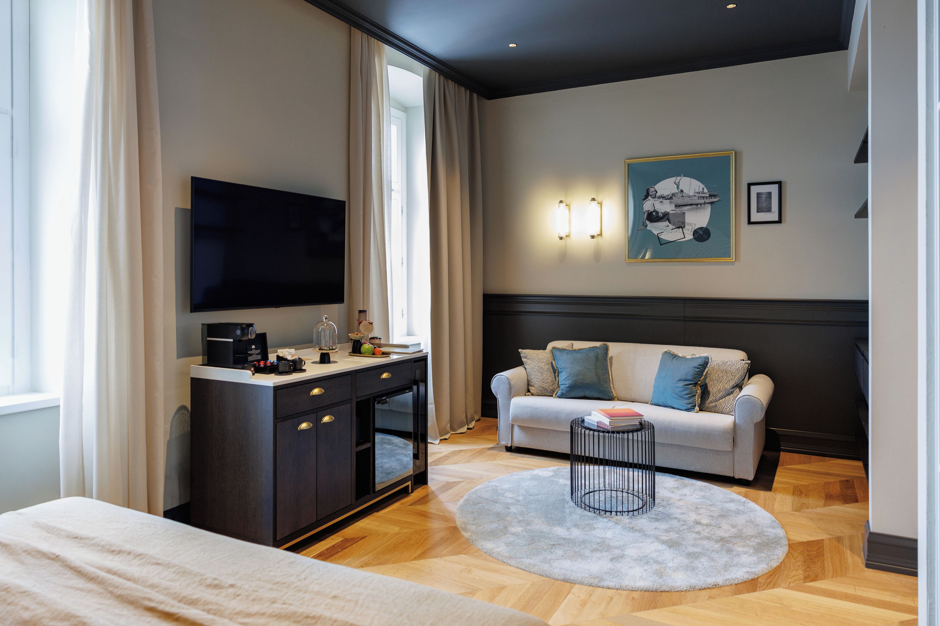 Una habitación de hotel moderna con una televisión de pantalla plana, un escritorio con cafetera, un sofá con cojines estampados y una alfombra redonda.