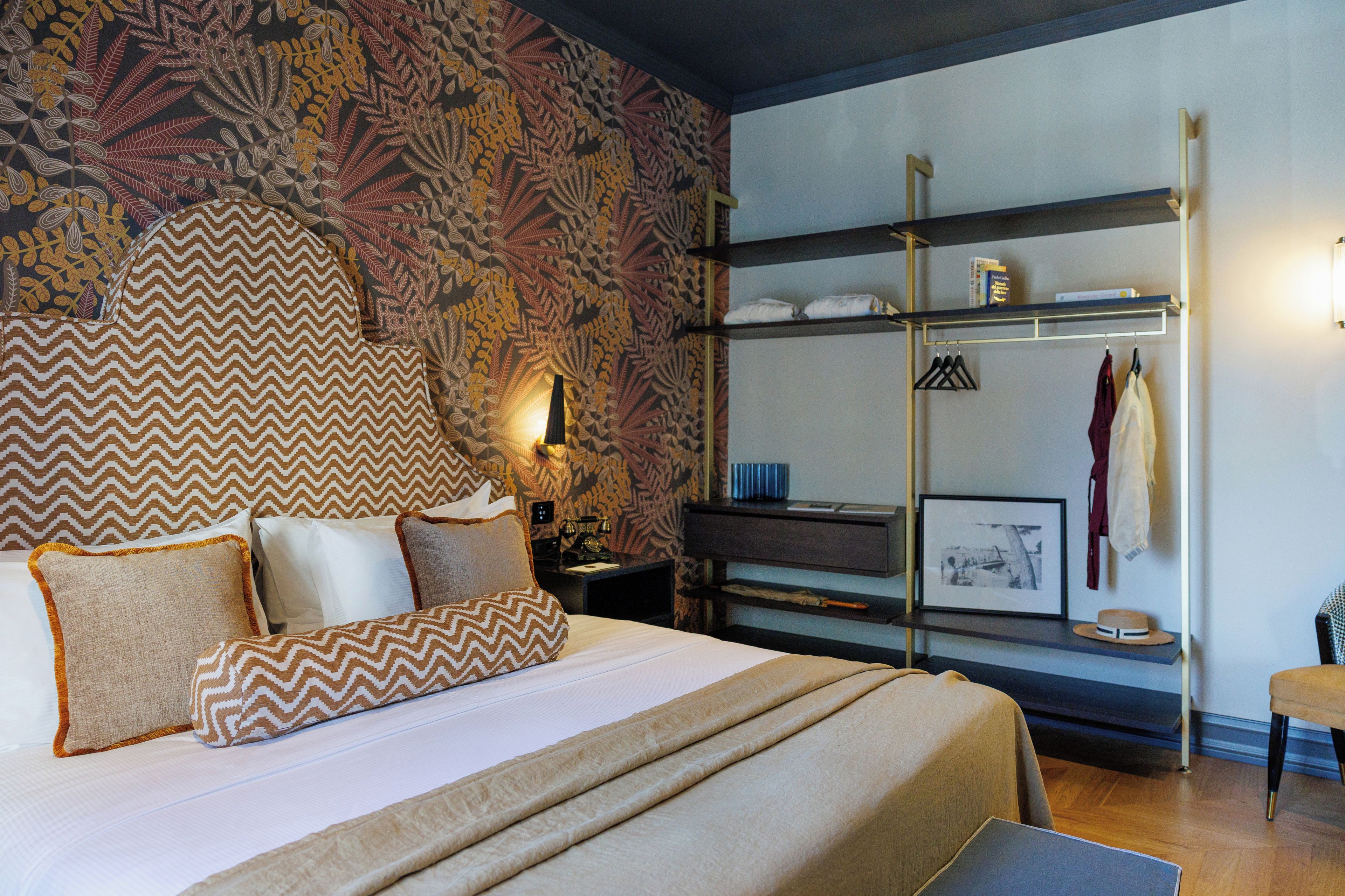 Habitación de hotel con cama, mesita de noche, lámpara, repisa con objetos y pared con diseño decorativo.