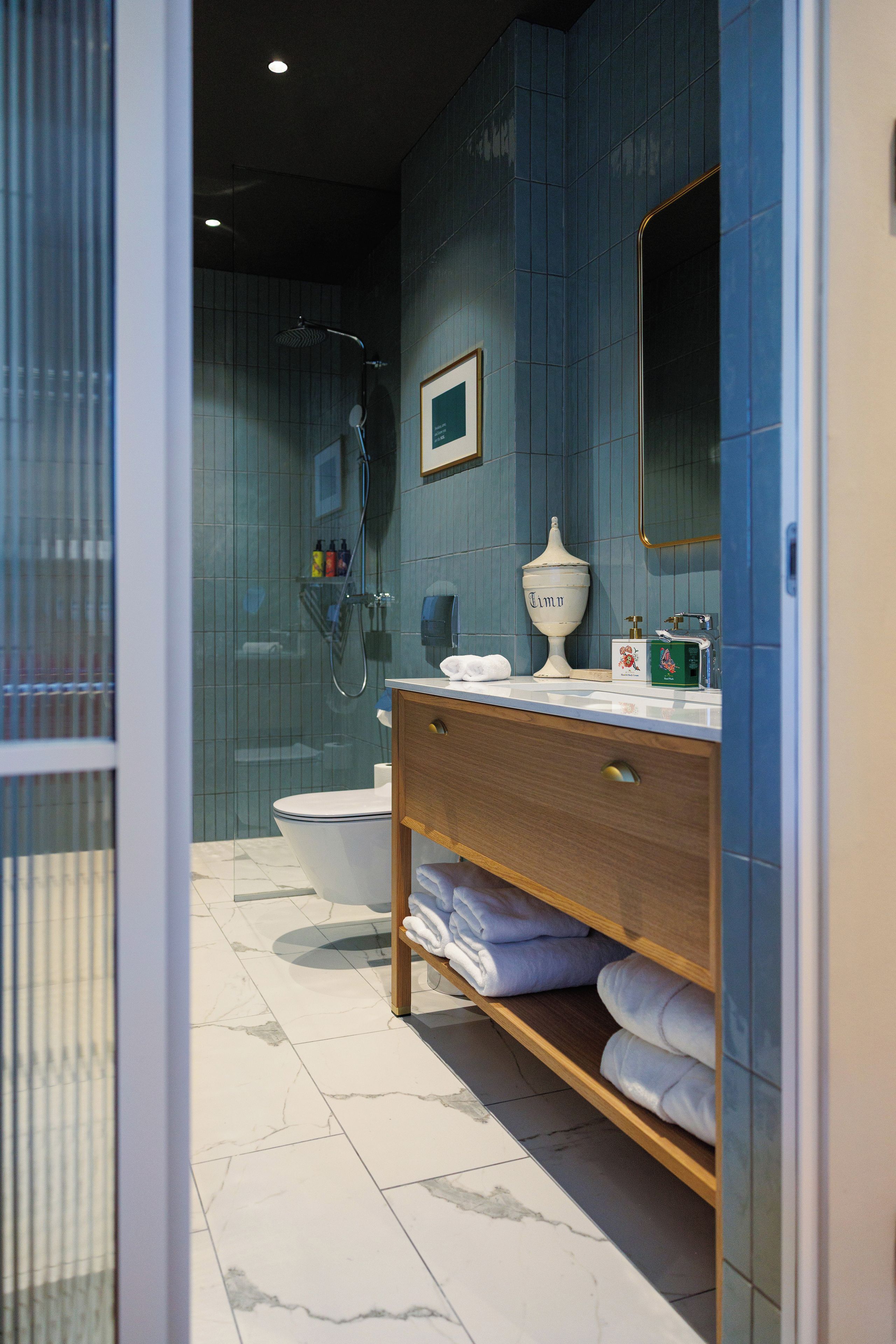 A modern bathroom with a glass shower enclosure, a toilet, a vanity with a mirror, and a shelf with towels.