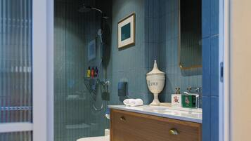 A modern bathroom with a glass shower enclosure, a toilet, a vanity with a mirror, and a shelf with towels.