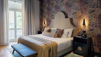 Ein Schlafzimmer mit einem großen Bett, zwei Nachttischen, einer Bank und Blick ins Freie durch ein Fenster.