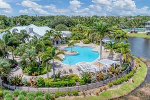 A resort with a central swimming pool, surrounded by palm trees and a lake. - Luxury 3BR Townhome - 10 min from Beach - 2 Master Suites - Private Elevator  (Placida)
