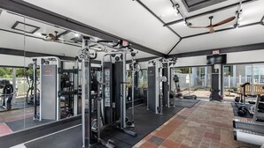 Un gimnasio con diversos equipos de ejercicio, un espejo grande en la pared y un ventilador de techo.