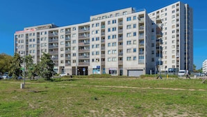 Un edificio residencial de varios pisos con balcones, entrada a nivel de calle y zona de estacionamiento.