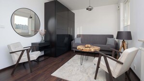 Una sala de estar moderna con piso de madera oscura, un espejo redondo, un sofá gris, dos sillones blancos, una mesa de centro de madera y una lámpara negra.
