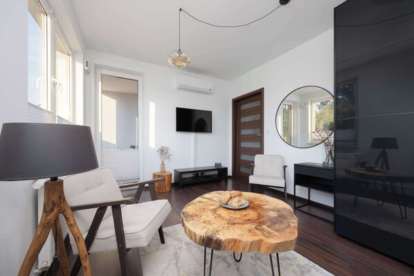A modern living room with a round wooden coffee table, a white sofa, a large floor lamp, a flat-screen TV, and a mirror.