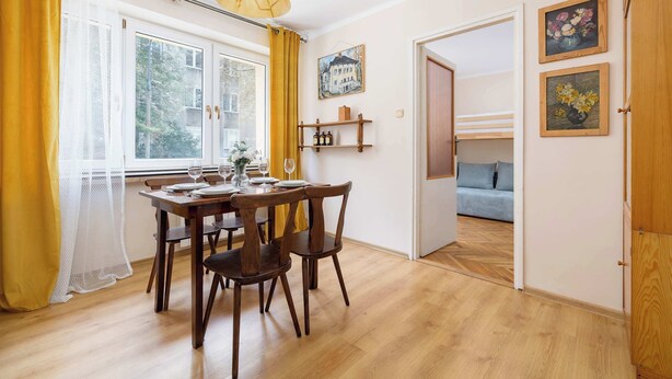 Ein Essbereich mit einem Holztisch und Stühlen, einem Fenster mit gelben Vorhängen und einem Bild an der Wand.