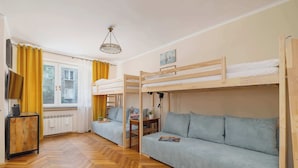 Ein Zimmer mit zwei Etagenbetten, einer Schlafcouch, einem Holztisch, einem Fernseher und einem Fenster mit Vorhängen.