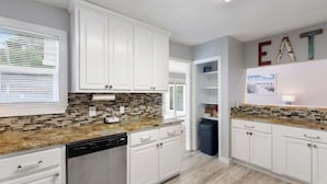 Cozinha moderna com armários brancos, bancada de granito e painel de azulejos mosaicados.