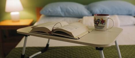 A bed with a green quilt, a bedside table with a lamp, and a mug on a small table beside the bed.