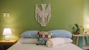 A neatly made bed with a macrame wall hanging, a patterned throw pillow, and a bedside lamp.