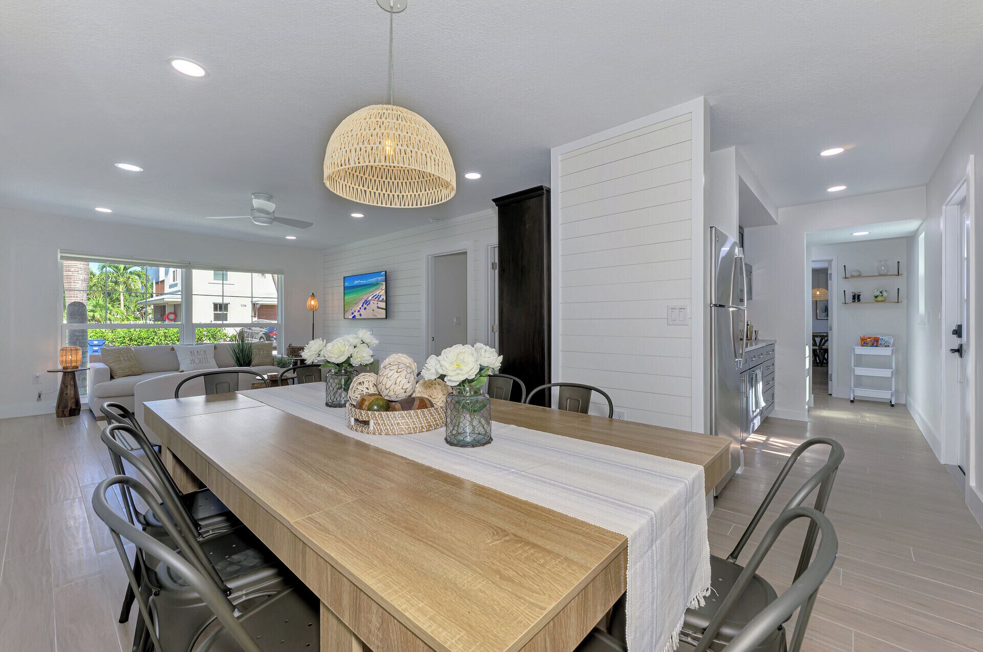 A modern dining area with a wooden table, white chairs, and a hanging light fixture.