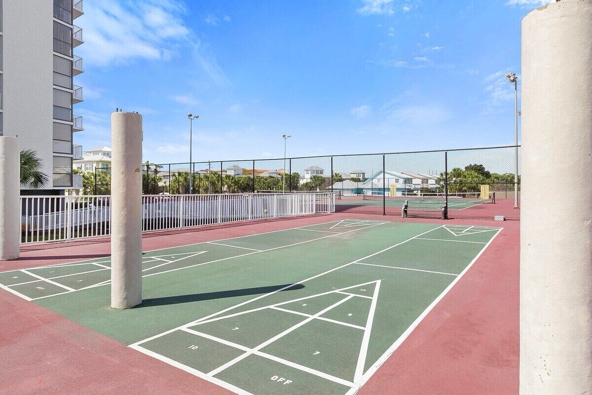 Una cancha de shuffleboard con superficie verde, líneas blancas delimitadoras y un borde rojo.