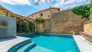 Ein Swimmingpool mit Steinwänden und ein Steinhaus im Hintergrund.