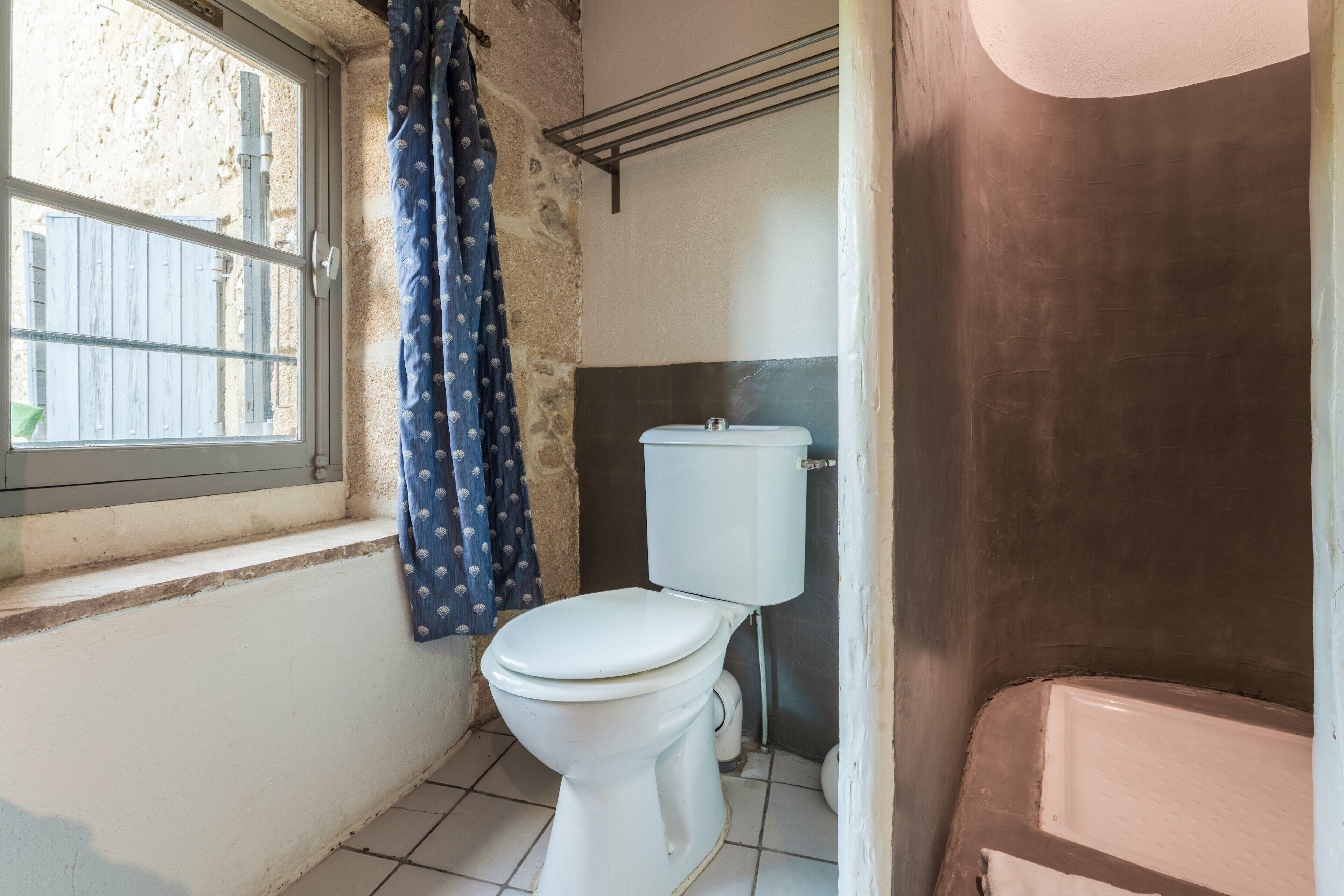 A bathroom with a toilet, a window with a curtain, and a bathtub.