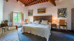 A bedroom with a wooden ceiling, a bed with striped bedding, a nightstand with a lamp, a chair, and two paintings on the wall. - Indigo Room with Shared Pool, Wi-Fi & Air Conditioning (Collias)