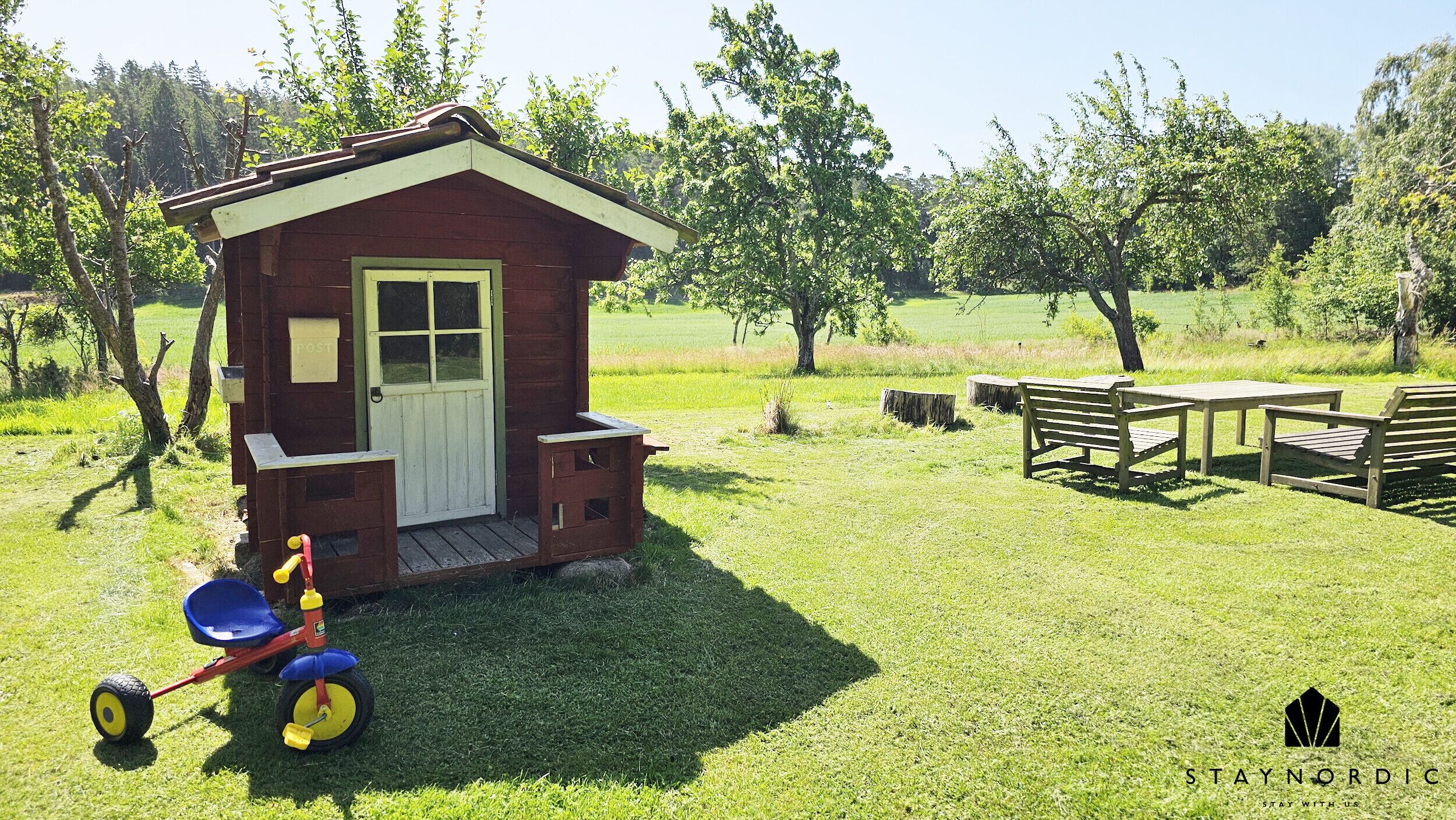 A small wooden cabin with a porch, a table and benches, and a tricycle nearby.