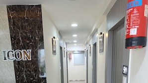 Zona de recepción de un hotel con un mostrador de mármol, un extintor y un pasillo que conduce a los ascensores.