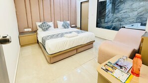 Una habitación de hotel moderna con una cama grande, una zona de estar y un baño con ducha de mármol.
