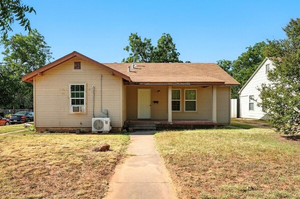 A single-story house with a front porch, a visible air conditioning unit, and a clear pathway leading to the entrance.