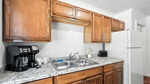 Eine Küche mit Holzschränken, einer Granit-Arbeitsplatte, einer Spüle, einer Kaffeemaschine und einem Kühlschrank.