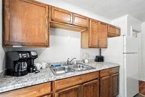 Eine Küche mit Holzschränken, einer Granit-Arbeitsplatte, einer Spüle, einer Kaffeemaschine und einem Kühlschrank.