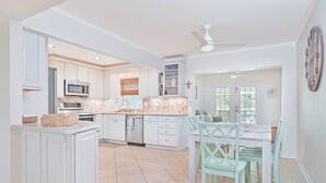 A modern kitchen with white cabinetry, a microwave, and a dining area with teal chairs and a white table. - Relax at Coral Cove – Poolside Paradise in Bonita Springs (Bonita Springs)