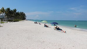 A wide sandy beach with palm trees, beach umbrellas, and people relaxing. - Relax at Coral Cove – Poolside Paradise in Bonita Springs (Bonita Springs)