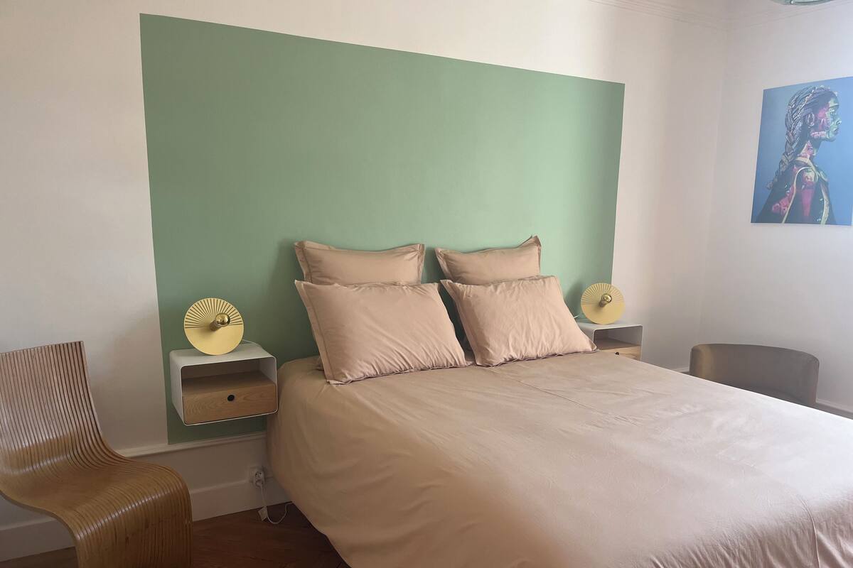 Une chambre à coucher comprenant un lit, deux tables de chevet, une chaise et un ventilateur fixé au mur.
