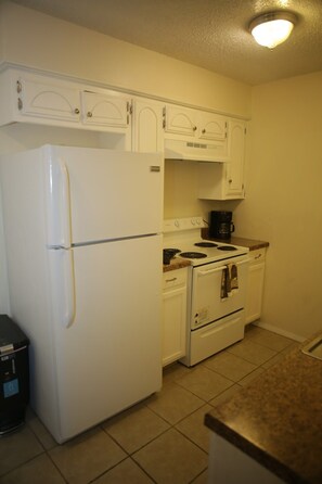 A compact kitchen with a white refrigerator, stove, and oven. There is a coffee maker on the countertop.
