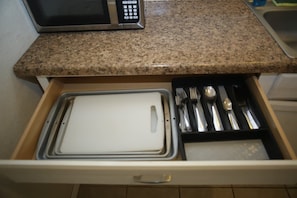 Un cajón de cocina con un microondas, utensilios y una tabla de cortar.