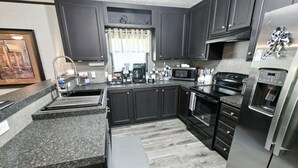 Eine moderne Küche mit dunklen Schränken, Granit Arbeitsplatten, einer Kaffeestation, einer Mikrowelle, einem Backofen und einem Kühlschrank.
