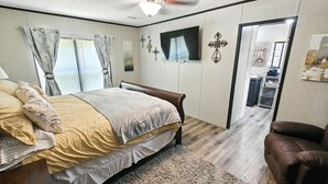 Ein Schlafzimmer mit Bett, Deckenventilator, Fernseher und einer Tür zu einem weiteren Raum.