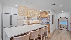 Una cocina moderna con una isla grande, armarios blancos y taburetes de mimbre.